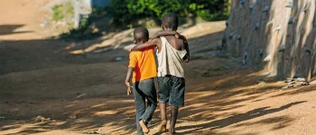 Zwei schwarze, barfüßig gehende, Kinder, Schulter an Schulter auf einem Sandweg