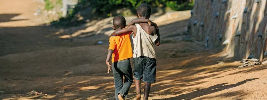 Zwei schwarze, barfüßig gehende, Kinder, Schulter an Schulter auf einem Sandweg